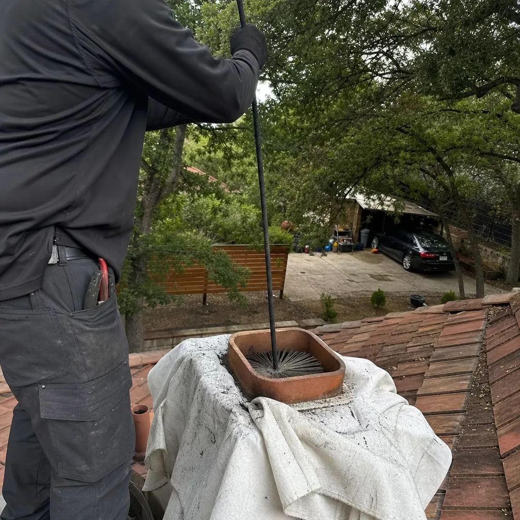 Professional chimney sweep cleaning a fireplace flue from the rooftop